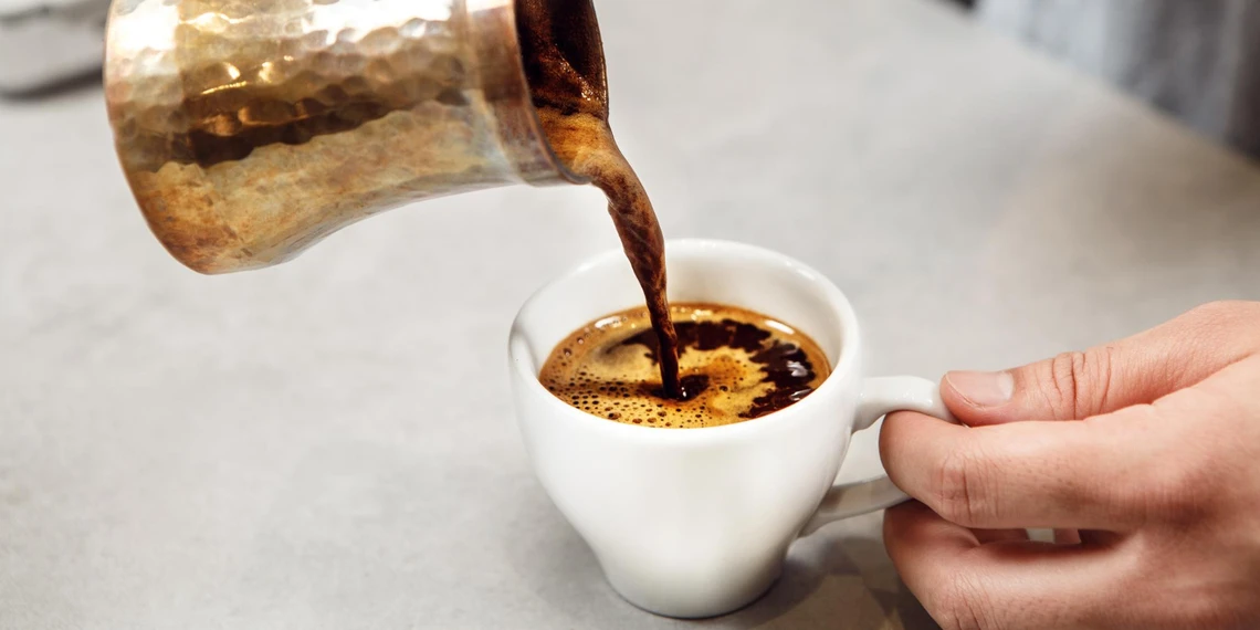 Pouring Turkish coffee from ibrik into traditional coffee cup