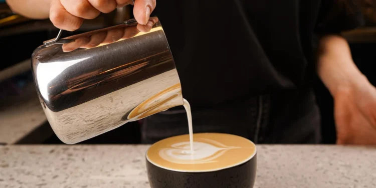 Barista using stainless steel milk pitcher to create latte art foam